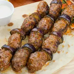 Kofta kebab z bakłażanem na płaskim chlebie, podany z sosem.
