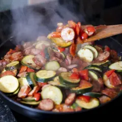 Gorące leczo składniki: cukinia, kiełbasa i papryka duszona na patelni, unosząca się para.