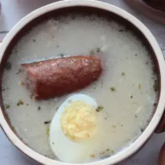 Aromaticzny żurek z kiełbasą i jajkiem, gotowy do podania. W tle czosnek, cebula i jajka, składniki idealnego zakwasu na żurek.