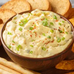 Kremowy dip z zieloną cebulką i papryką, otoczony chrupiącymi grzankami, nachos i paluszkami. Idealny do zanurzania!