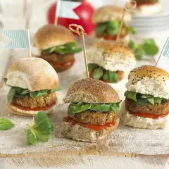 Mini burgery z kotletem, sałatą i flagietkami na desce.