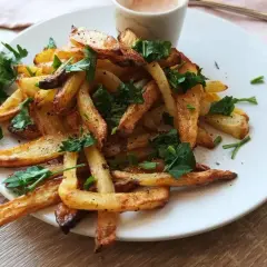 Chrupiące frytki posypane natką pietruszki, gotowe do zanurzenia w pysznym sosie do frytek.