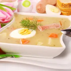 Biały barszcz przepis babci, z jajkiem i kiełbasą, ozdobiony koperkiem. W tle pisanki i tulipany.