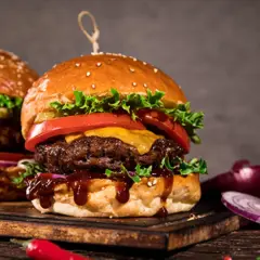 Dwa soczyste burgery z serem, sałatą i pomidorem na desce, obok cebuli i papryczki chili.