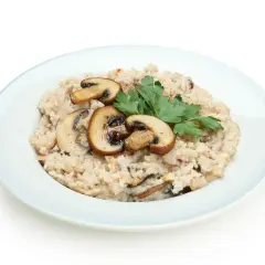 Kremowy ryż do risotto z pieczarkami i natką pietruszki na jasnoniebieskim talerzu.