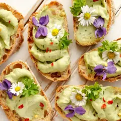 Pyszne **finger food**: grzanki z awokado, ozdobione kwiatami i ziołami. Idealne na wiosenne przyjęcie.