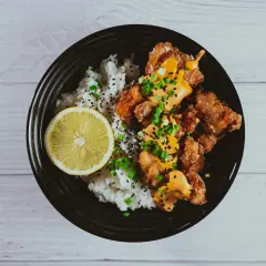 Chrupiące karaage z ryżem, polane sosem i posypane szczypiorkiem, z plasterkiem cytryny.