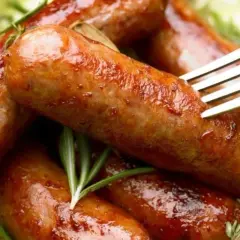 Soczysta kiełbasa z piekarnika, rumiana i aromatyczna, podana z gałązkami rozmarynu. Widok zachęca do spróbowania.