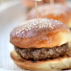 Mini burger z sezamową bułką i kotletem na talerzu.