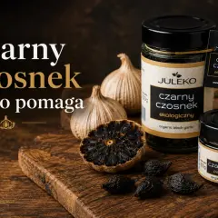 Czarny czosnek Juleko na desce. Słoiczki i ząbki czarnego czosnku, obok główki zwykłego czosnku.