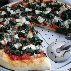 Pyszna pizza ze szpinakiem i białym serem, gotowa do pokrojenia.