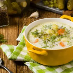 Zupa ogórkowa z koperkiem, ziemniakami i marchewką. W tle słoik z pieprzem, czosnek i ogórki kiszone – idealne jakie przyprawy do zupy ogórkowej.