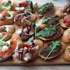 Tanie przekąski na imprezę: bruschetty z łososiem, szynką parmeńską, pastą z oliwek i pomidorami. Idealne na każdą okazję!