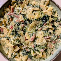 Pyszny makaron farfalle w kremowym sosie ze szpinakiem mrożonym i kawałkami boczku.