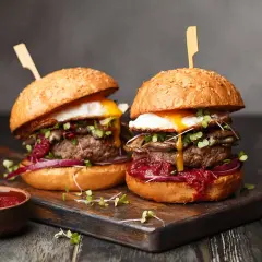 Dwa soczyste burgery z grilla z jajkiem sadzonym, grzybami i czerwoną cebulą, podane z sosem.
