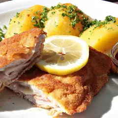 Pyszny kotlet po szwajcarsku, podany z ziemniakami, plasterkiem cytryny i żurawiną.