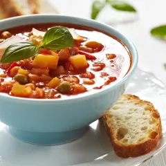 Aksamitna zupa solferino w błękitnej misce, udekorowana bazylią i parmezanem, obok kromka chleba.