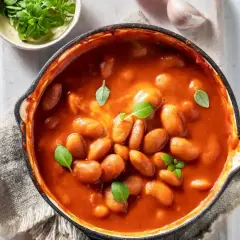 Pyszna zupa fasolowa przepis babci w garnku, udekorowana bazylią. Obok pomidor i czosnek.