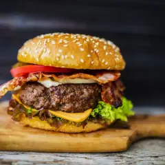 Soczysty burger z wołowiny z bekonem, serem, pomidorem i sałatą na desce.
