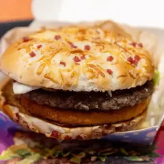 Apetyczny burger drwala z chrupiącą bułką posypaną serem i kawałkami boczku, w środku soczysty kotlet i panierowany dodatek.