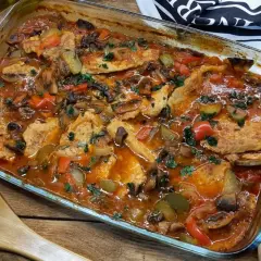 Schab po cygańsku z pieczarkami i papryką w sosie pomidorowym, posypany natką pietruszki, w szklanym naczyniu żaroodpornym.