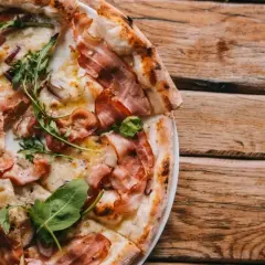 Pyszna pizza carbonara z chrupiącym boczkiem i rukolą, podana na drewnianym blacie.