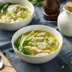 Dwie miseczki aromatycznej zupy won ton z zielonymi warzywami i posiekanym szczypiorkiem.
