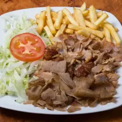 Talerz z prawdziwym kebabem, frytkami, sałatą i pomidorem. Apetyczny posiłek na drewnianym blacie.
