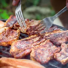Soczysty boczek na grillu, idealny po marynacie. Dwie widelce sprawdzają stopień wysmażenia.