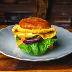 Soczysty burger z serem, sałatą, ogórkiem i czerwoną cebulą na talerzu.