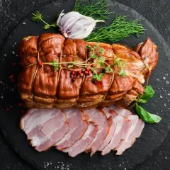 Wędzona szynka, idealna do wędzenia, prezentowana z czosnkiem i ziołami. Pokrojone plastry szynki obok.