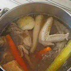 Gotowanie rosołu bez przykrycia. W garnku bulgoczą marchewki, kawałki kurczaka, skrzydełka, por i ziemniaki.