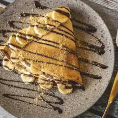 Pyszne naleśniki z bananami i czekoladą, posypane kruszonką. Idealne składniki na deser.