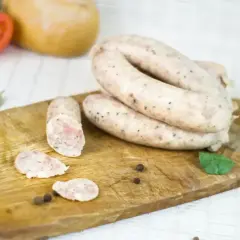 Biała kiełbasa na desce, gotowa do przygotowania według przepisu na 5 kg. W tle pomidor i cebula.