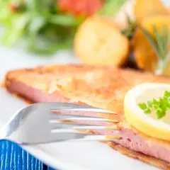 Kotlety z mortadeli w panierce, podane z ziemniakami, sałatką i plasterkiem cytryny.