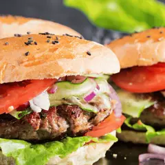 Dwa soczyste burgery wołowe z bułką, pomidorem, sałatą i ogórkiem.