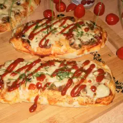 Dwa podłużne, zapieczone ciasta na pizzę z serem, pieczarkami i keczupem, ozdobione szczypiorkiem.