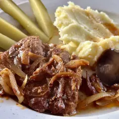 Karkówka z piekarnika w plastrach, duszona z cebulką, podana z puree ziemniaczanym, ogórkami kiszonymi i pieczarką.