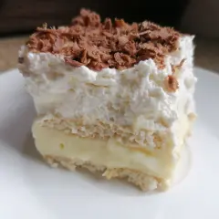 Szybkie ciasto bez pieczenia z budyniem i herbatnikami, przełożone kremem i posypane czekoladą. Idealne na deser!