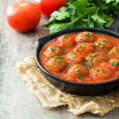 Pyszne pulpeciki w aromatycznym sosie pomidorowym, posypane natką pietruszki. Idealny sos do pulpetów na drewnianym stole.