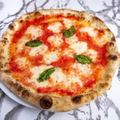 Pyszna pizza napoletana z pomidorami, mozzarellą i bazylią na białym talerzu, na tle marmurowego wzoru.