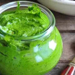 Słoik pełen intensywnie zielonego pesto z pietruszki, gotowego do użycia. Obok leży złota łyżeczka.