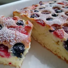 Puszyste ciasto na maślance z jagodami i malinami, posypane cukrem pudrem.