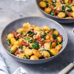 Pyszne gnocchi ze szpinakiem, suszonymi pomidorami i orzeszkami pinii, posypane parmezanem.