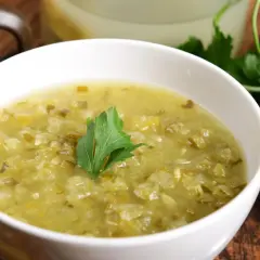Zupa ogórkowa przepis babci. Aromatyczna, domowa zupa z kiszonych ogórków, podana w białej miseczce z gałązką natki pietruszki. Obok leżą ogórki kiszone.