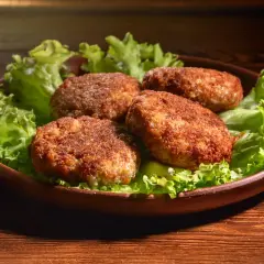 Cztery apetyczne kotlety mielone z airfryer, podane na liściach sałaty, prezentują się wyśmienicie.
