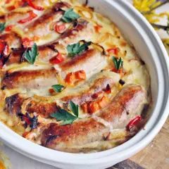 Biała kiełbasa w sosie chrzanowo-musztardowym, zapieczona z warzywami i ziołami, prezentuje się apetycznie w naczyniu.