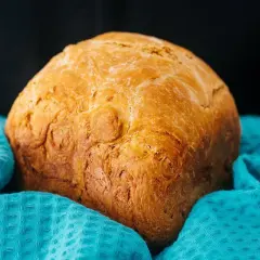 Złocisty chleb z airfryer, pachnący świeżością, otulony turkusowym ręcznikiem. Idealny na śniadanie.