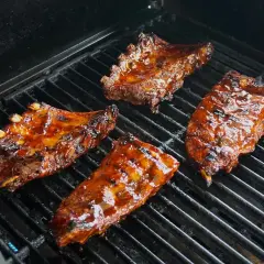 Soczyste żeberka w marynacie do żeberek skwierczą na grillu, nabierając apetycznego koloru.