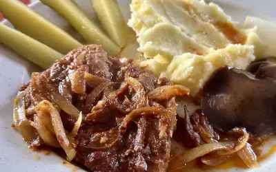 Karkówka z piekarnika w plastrach, duszona z cebulką, podana z puree ziemniaczanym, ogórkami kiszonymi i pieczarką.